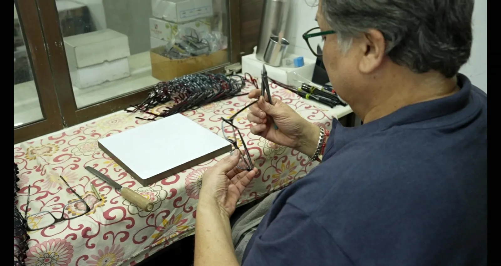 Quality control specialist measuring acetate optical frame dimensions at inspection bench