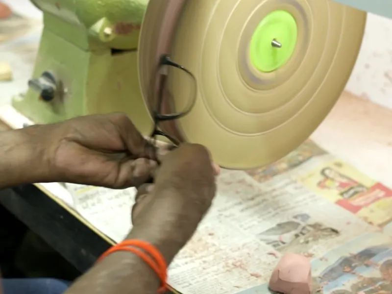 Master artisan hand polishing organic cellulose acetate optical frame edges on a high-speed pumice buffing wheel