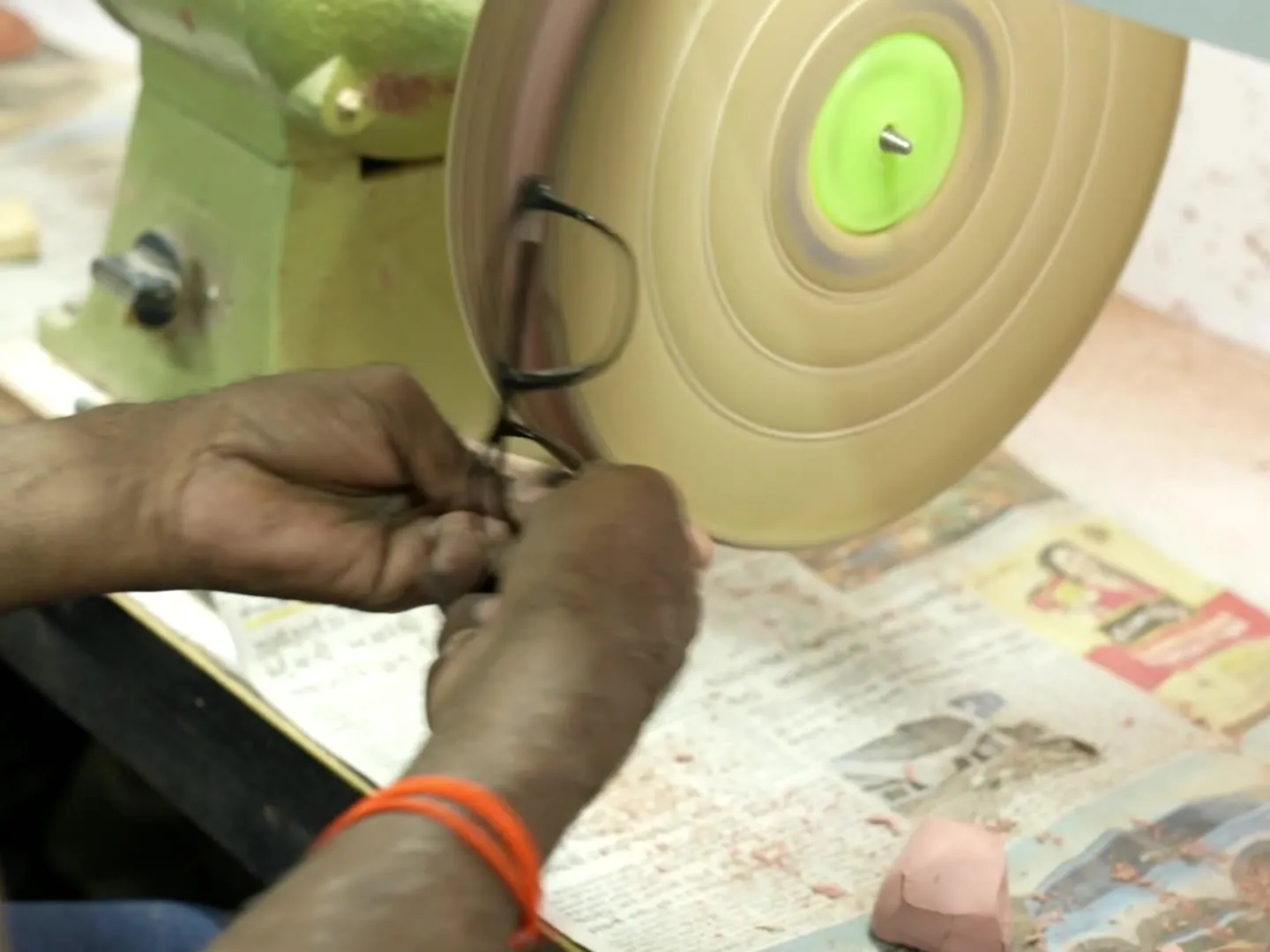 Artisan hand working the bridge area of an acetate frame front on an optical polishing wheel